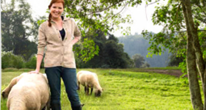 Photo d'une femme posant avec deux moutons en arrière plan sur fond de paysage bucolique