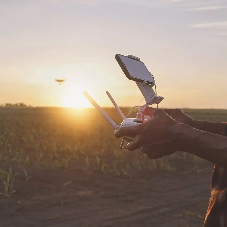 Photo d'un homme tenant une manette de contrôle d'un drone dans un champ au couché du soleil